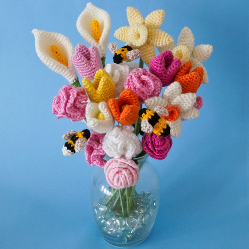 A vase filled with a variety of cheerful crocheted flowers and Tiny Bees, all crochet patterns by June Gilbank