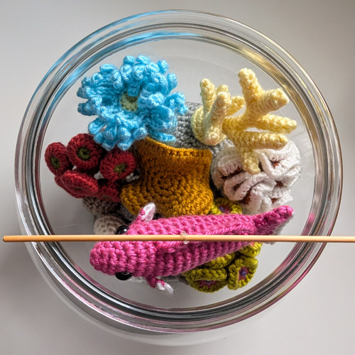 glass fishbowl with crocheted corals and a suspended tropical fish, seen from the top, all made from PlanetJune patterns