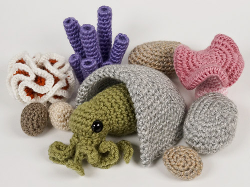 baby amigurumi octopus peeking out of a crocheted cave surrounded by crocheted rocks and corals, all made from PlanetJune patterns